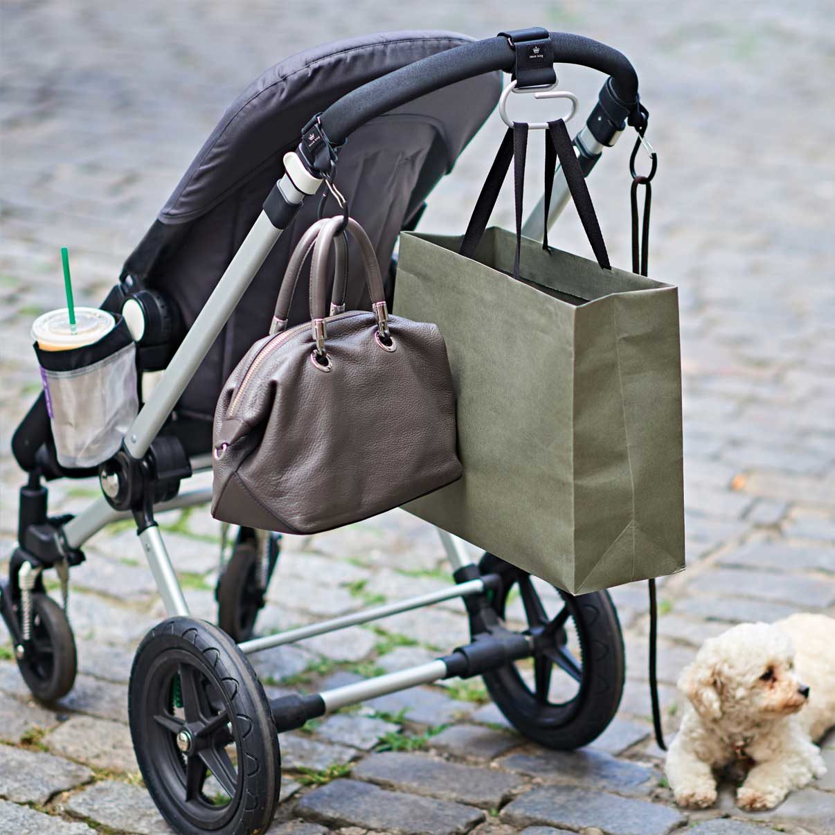 Stroller with Think King hooks holding bags, cup holder with iced coffee, and dog leash on a clippy hook